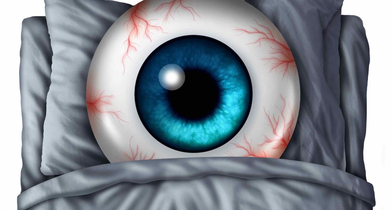 Insomnia and sleeping problems concept as a human eye ball with red veins in a bed with a pillow as a symbol of the health risks of nighttime sleeplessness disorder.